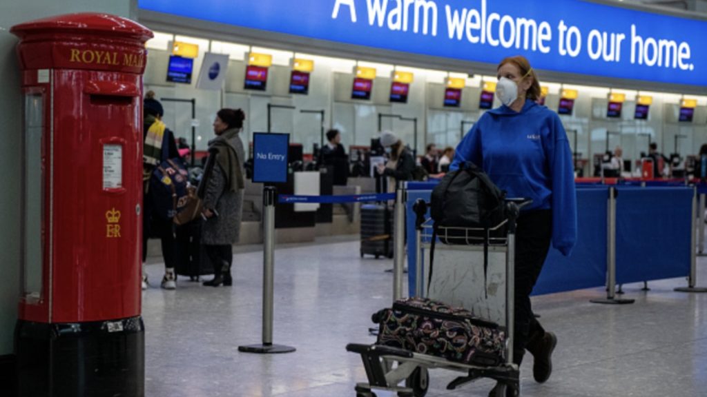 An airline passenger wearing a face mask pushes her bags past a post box at Heathrow Terminal 5 departures as the outbreak of coronavirus intensifies on March 15, 2020 in London
