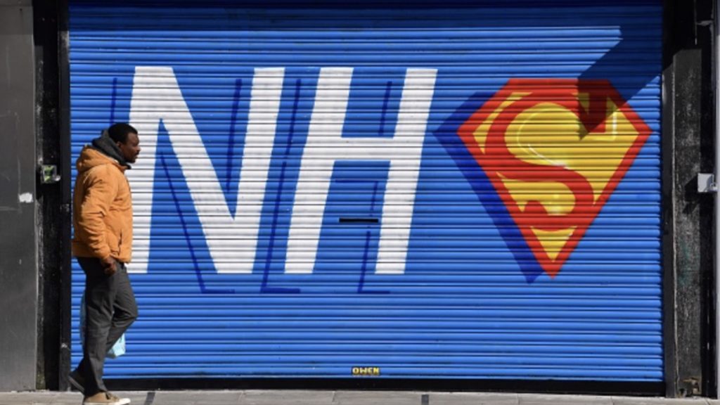 A pedestrian walks past graffiti depicting the logo of Britain's NHS (National Health Service), merged with the emblem or badge of the fictional super heros Superman and Superwoman, on the shuttered entrance of a closed Pizza restaurant in Liverpool, north west England on April 20, 2020
