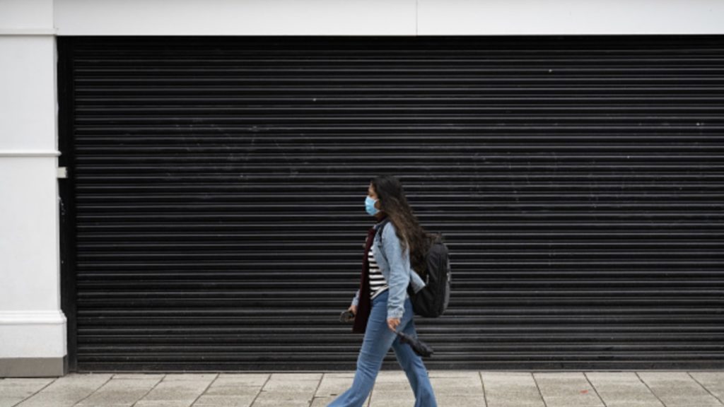 A woman walks passed the shutters of a closed shop on March 17, 2020 in Cardiff, Wales.