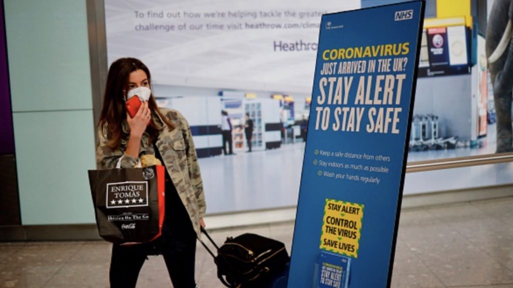 A newly arrived passenger wearing a face mask as a precaution against the novel coronavirus walks past a sign at Heathrow airport, west London, on May 22, 2020 with the British government's new 'Stay Alert' message on it.