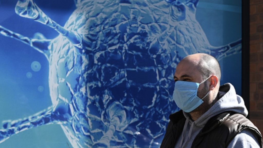 A man wearing a mask walks past the Regional Science Centre in Oldham, Lancashire on March 26, 2020, during a country-wide lockdown to slow the spread of the novel coronavirus COVID-19.